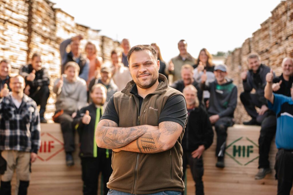 Ein Mitarbeiter steht mit verschränkten Armen vor den restlichen Mitarbeitern