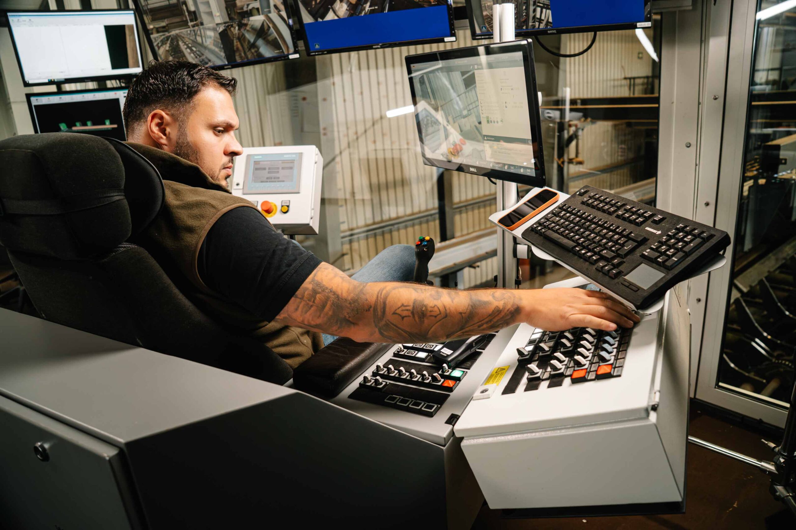 Ein Mann sitzt vor vielen Bildschirmen und Knöpfen, die die Säge steuern und drückt einen Kmopf